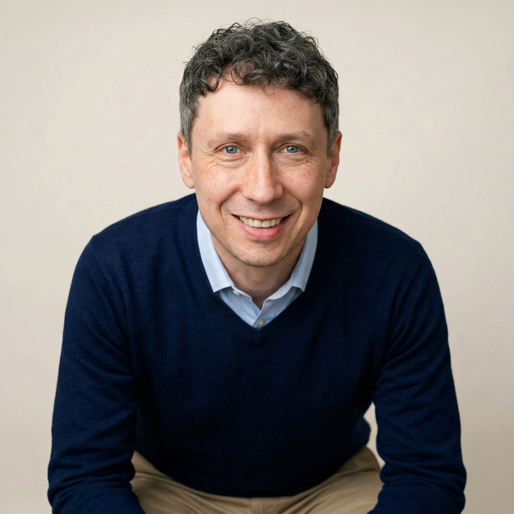 Kolia Bogumil mit blauem Pulli und Hemd, sitzend und leicht vorgebeugt